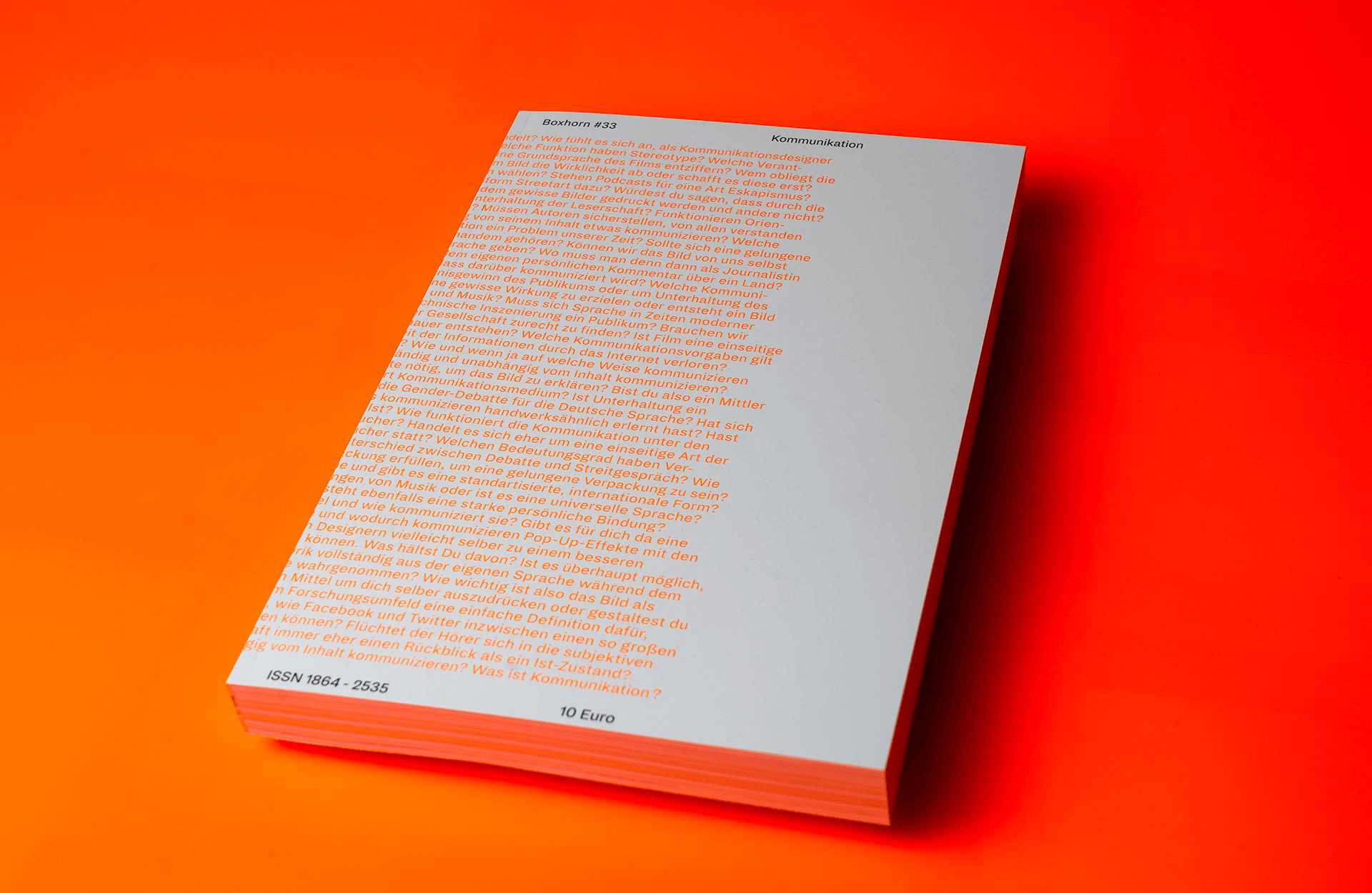 A white magazine in A4 size shown in perspective on a neon orange background.