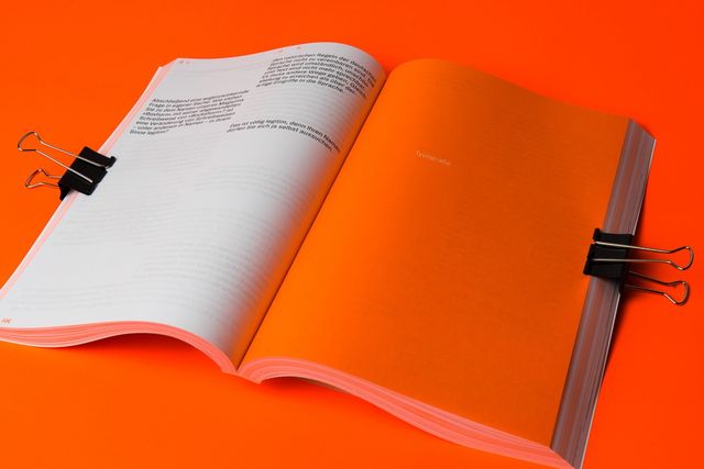A spread of a magazine the left shows text in two columns, the right shows a neon orange page. The photo is shot on a neon orange background.